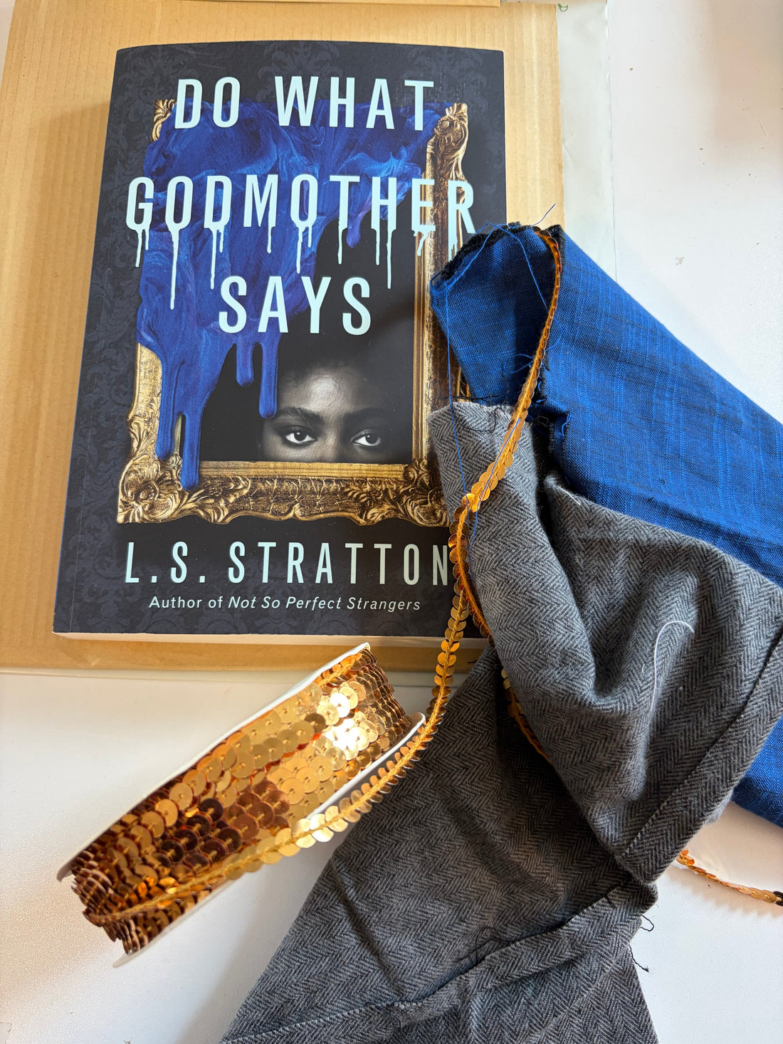 Blue linen, herringbone flannel, ribbon, and vintage buttons arranged beside a copy of Do What Godmother Says by L.S. Stratton.