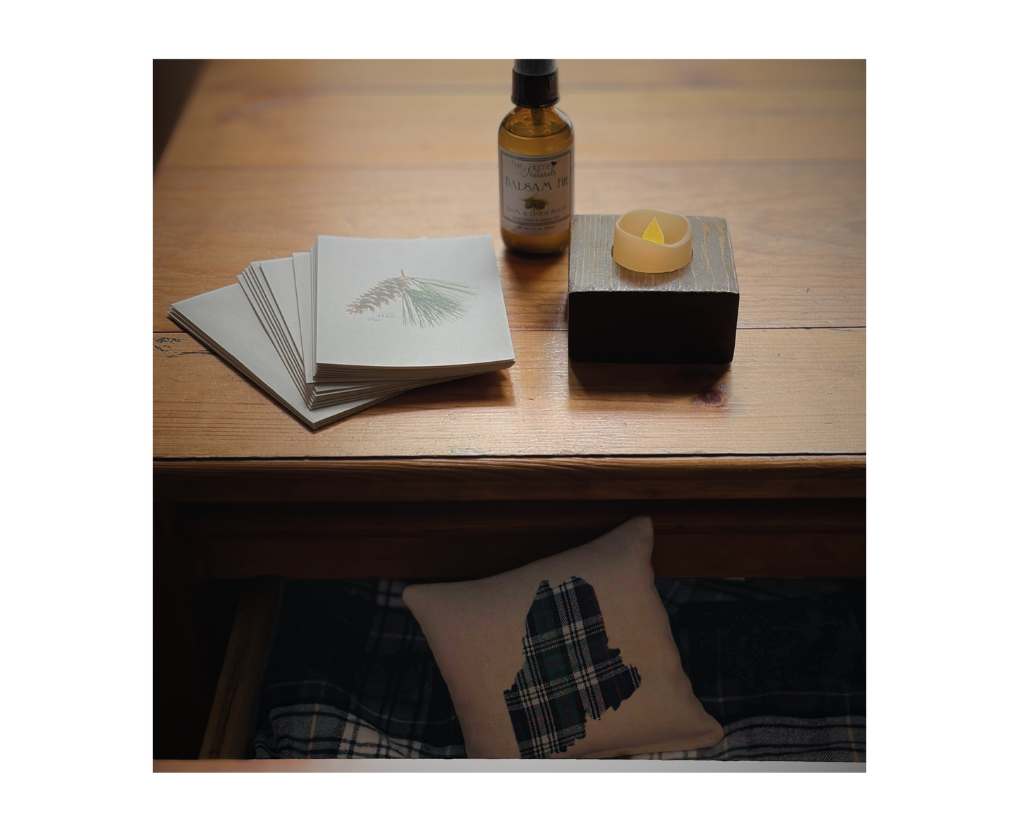 Small bottle of balsam fir room spray made with organic essntial oil, pine themed notecards with pinecone design, and a wooden handcrafted LED tealight holder, on top of a handmade wooden dresser. 